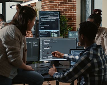 Programer-sitting-on-desk-discussing-with-mixed-team-of-software-developers-about-artificial-intelligence-innovation