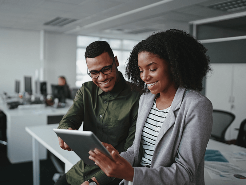 Smiling young African American professional businessman and businesswoman together working online with a digital tablet in office